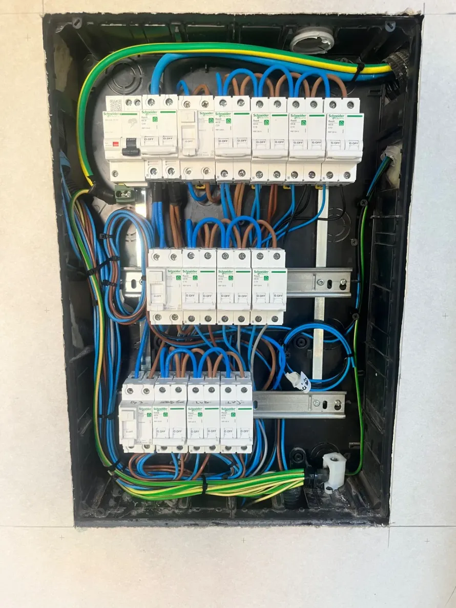 Panel eléctrico con filas de disyuntores, cables y cables de tierra. Los cables azul, marrón, verde y amarillo están organizados dentro de la caja negra.