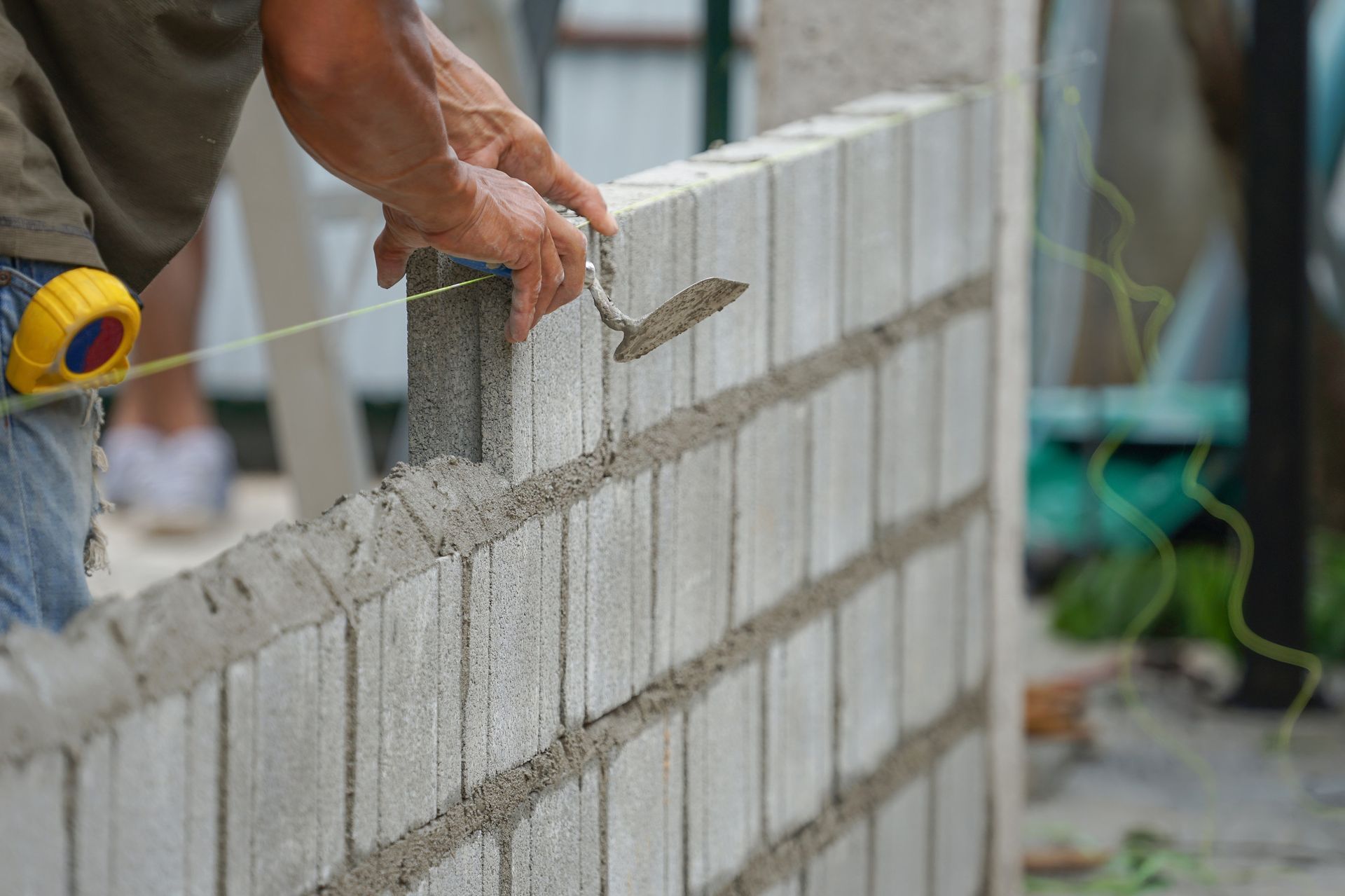 Un hombre está construyendo un muro de ladrillos con una paleta y una cinta métrica.