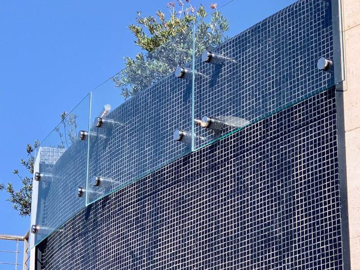 Un edificio con una valla de cristal y un árbol encima.