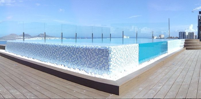 Una gran piscina encima de una terraza de madera con vista al océano.
