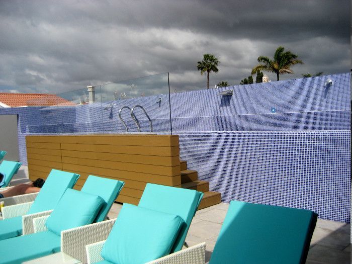 Una piscina con sillas azules y un cielo nublado al fondo.