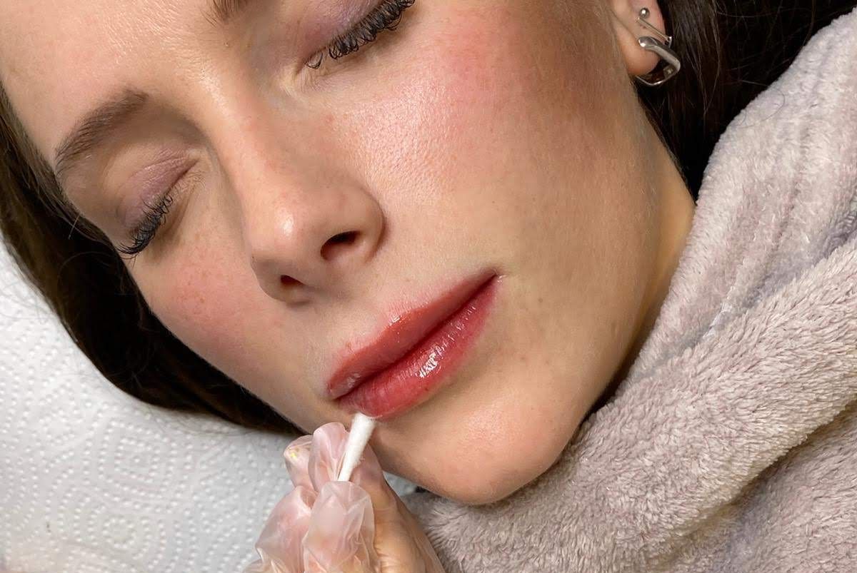 Eine Frau lässt sich von einem Visagisten die Lippen schminken.