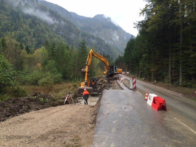 Travaux de construction routière en zone montagneuse. Une pelleteuse et des ouvriers réparent la chaussée