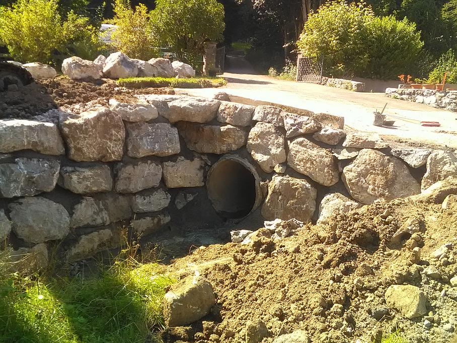 Logo bleu et blanc « TP Girod » sur fond d'enrochement d'un petit pont