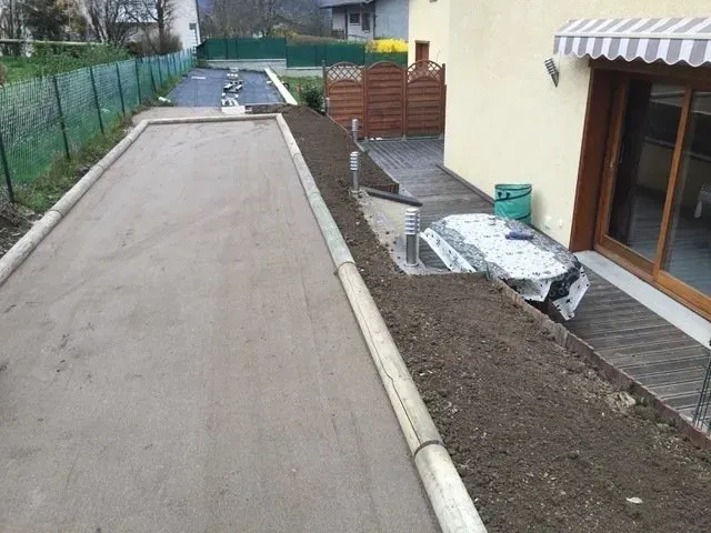 Terrain de pétanque en gravier jouxtant une maison avec un parterre de terre surélevé