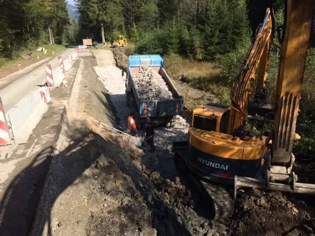Une excavatrice charge de la terre dans un camion-benne en bordure de route