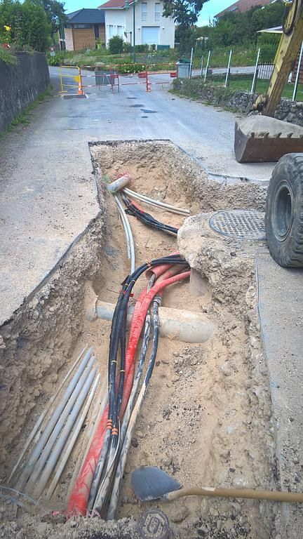 Tranchée dans la chaussée avec câbles et canalisations électriques apparents