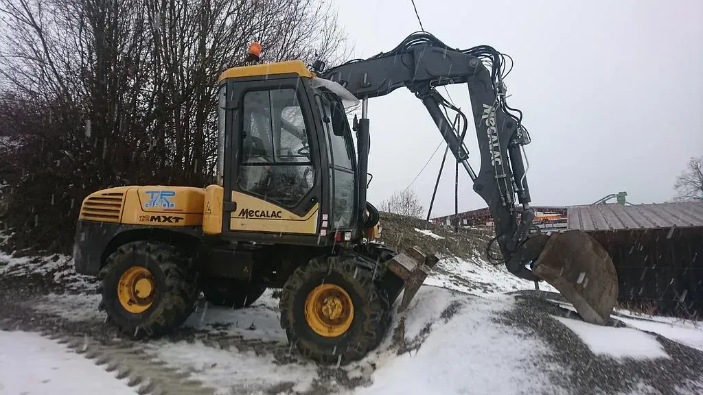 Une pelleteuse jaune et noire sur un sol enneigé, le bras tendu vers un tas de gravier