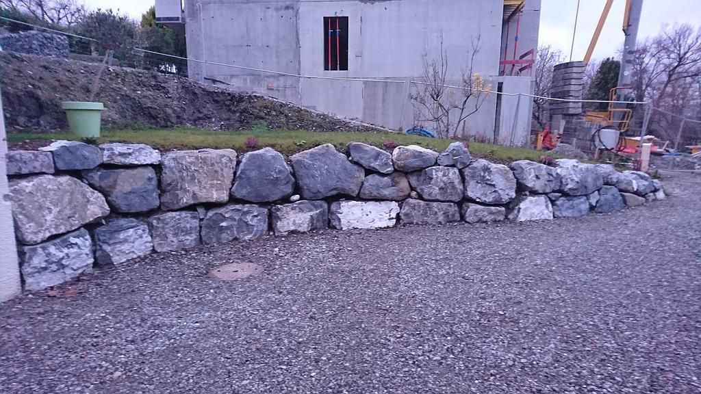 Mur de soutènement en pierre et allée de gravier devant un bâtiment en construction