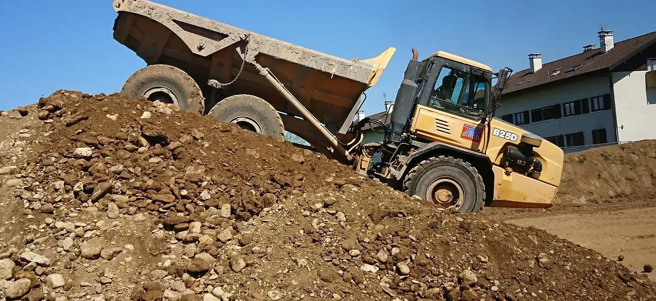 Un camion-benne jaune décharge de la terre sur un chantier de construction à côté d'un bâtiment