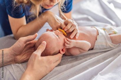 Un parent tient un bébé. On lui donne une tétine. Le bébé est allongé sur un lit, portant une couche.