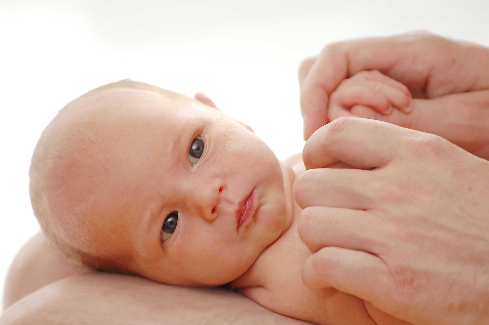 Bébé tenu par des mains d'adultes ; peau claire, regardant la caméra.