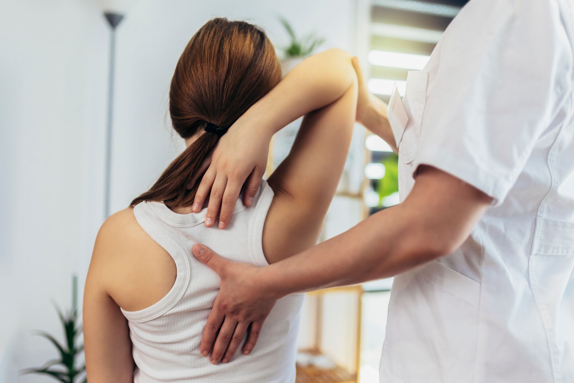 Une femme en débardeur blanc reçoit un ajustement d'épaule de la part d'une personne en blouse blanche.