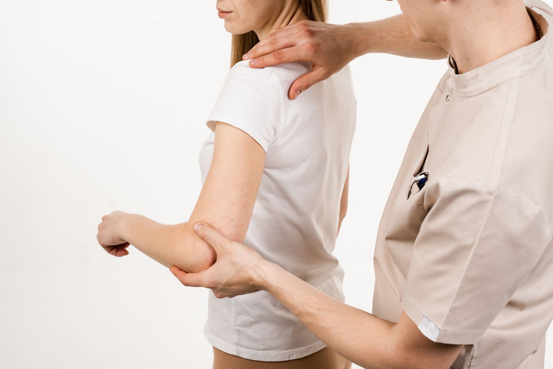 Un médecin examine le bras d'une femme, vérifiant son épaule et son coude, dans une pièce aux murs blancs.