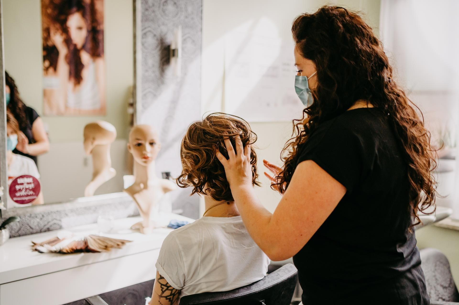 Eine Friseurin mit Mundschutz stylt im Salon die kurzen, lockigen Haare einer Kundin.
