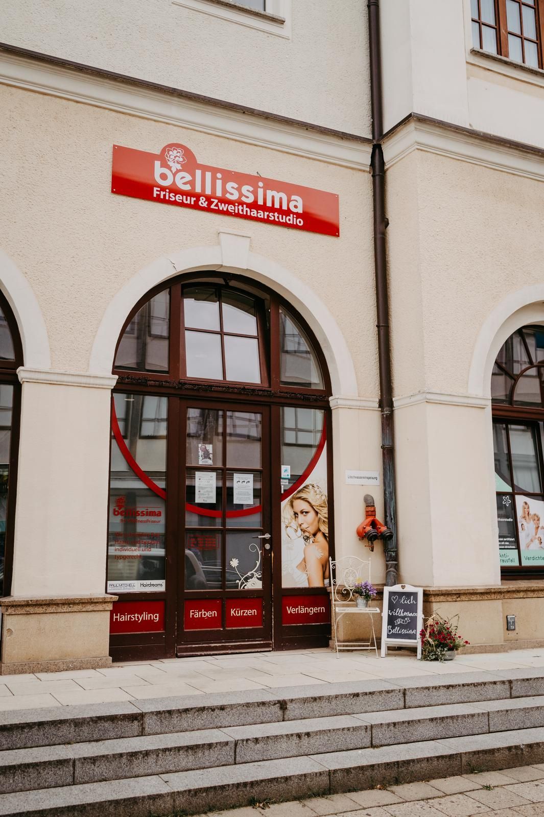 Bellissima Parfümeriegeschäft mit roter Beschilderung, gewölbtem Eingang und Steintreppe.