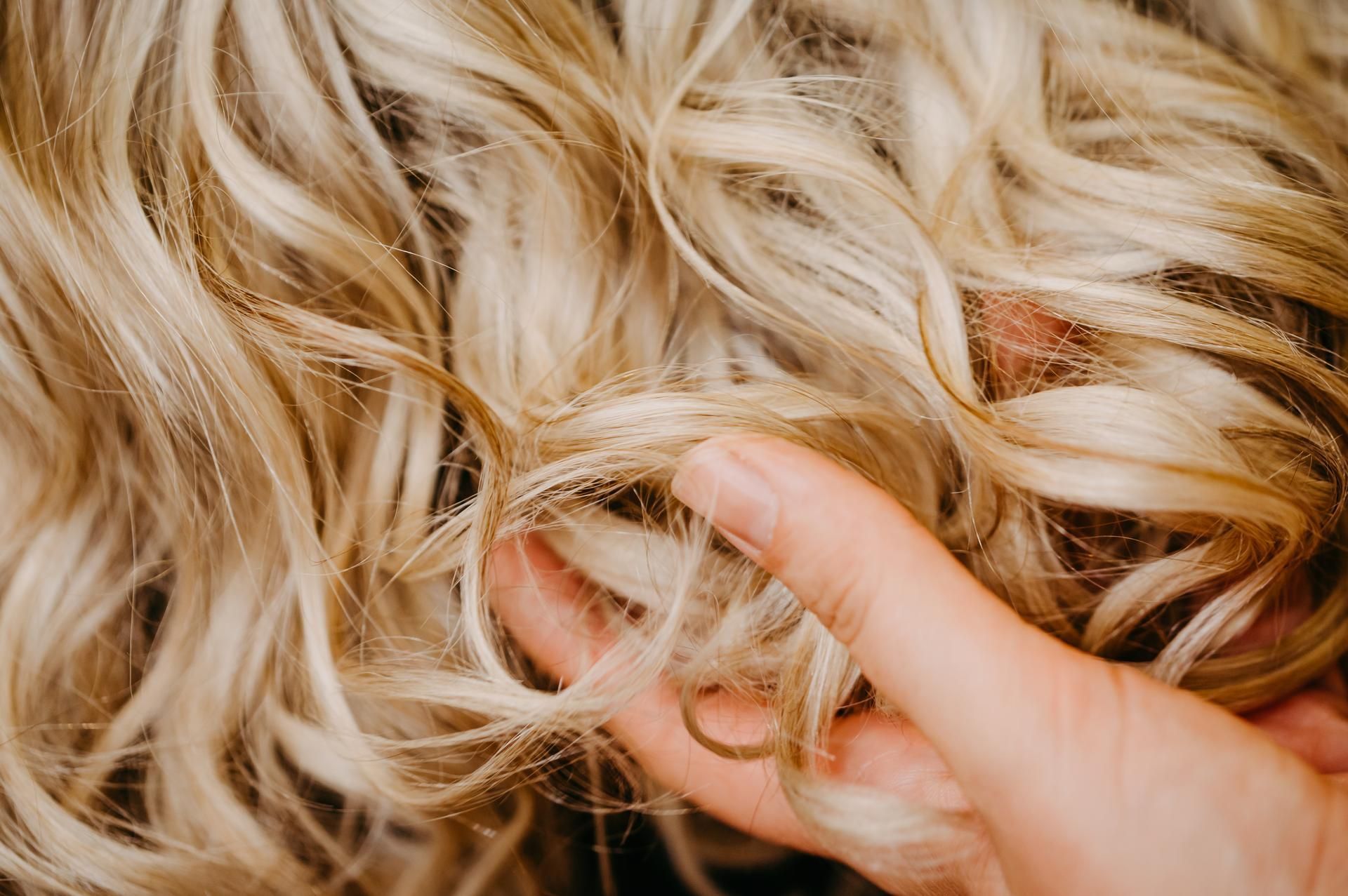 Eine Hand berührt welliges, hellblondes Haar.