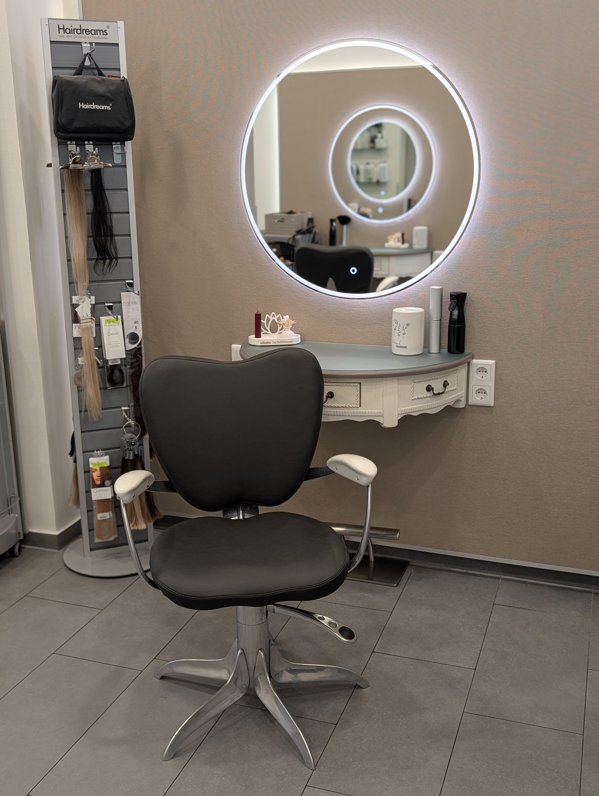 Friseursalon-Arbeitsplatz mit Stuhl, Spiegel und Produktpräsentation. Grau-, Weiß- und Brauntöne.