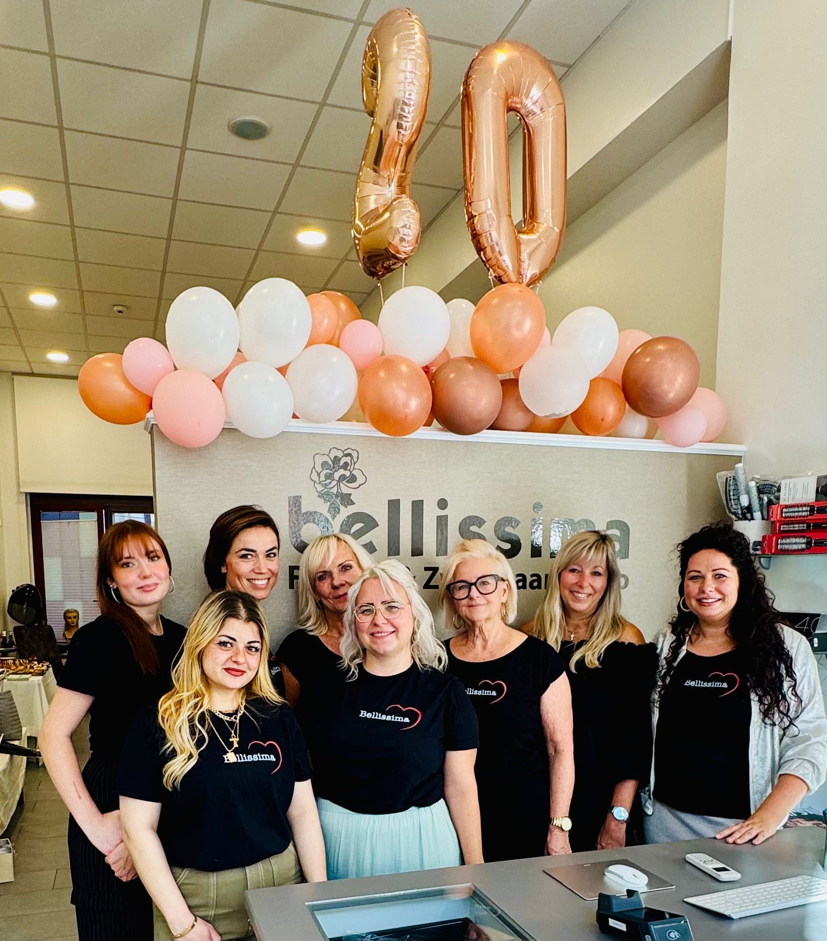 Eine Gruppe von Frauen in schwarzen Hemden feiert in einem Salon mit Luftballons, die die Zahl „80“ bilden.