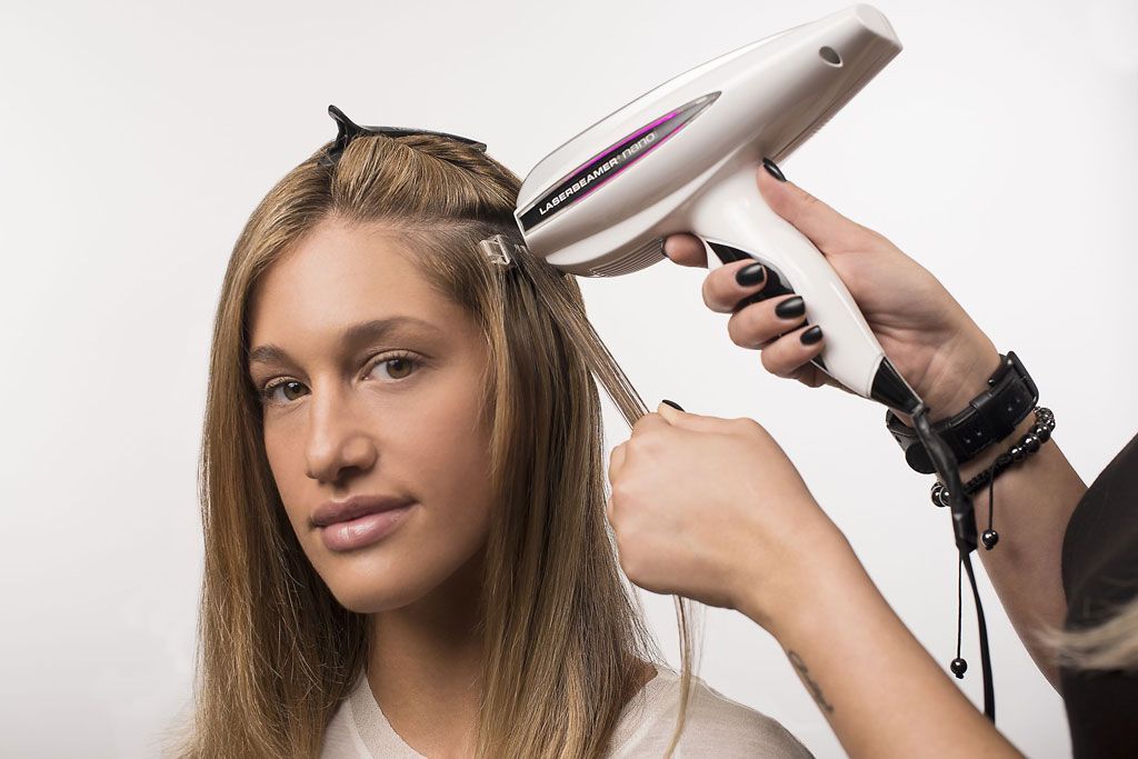 Eine Person lässt sich mit einem Gerät Haarverlängerungen anbringen. Blondes Haar, weißer Hintergrund, Nahaufnahme.