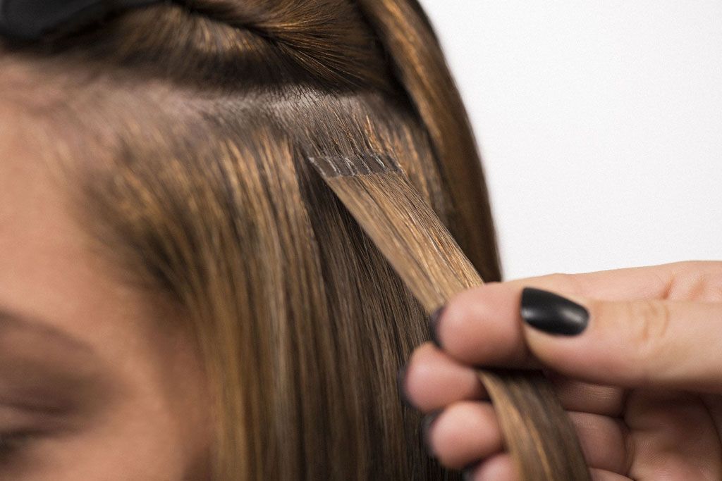 Eine Hand hält Haarsträhnen mit daran befestigten Haarverlängerungen in blonden und braunen Farbtönen.