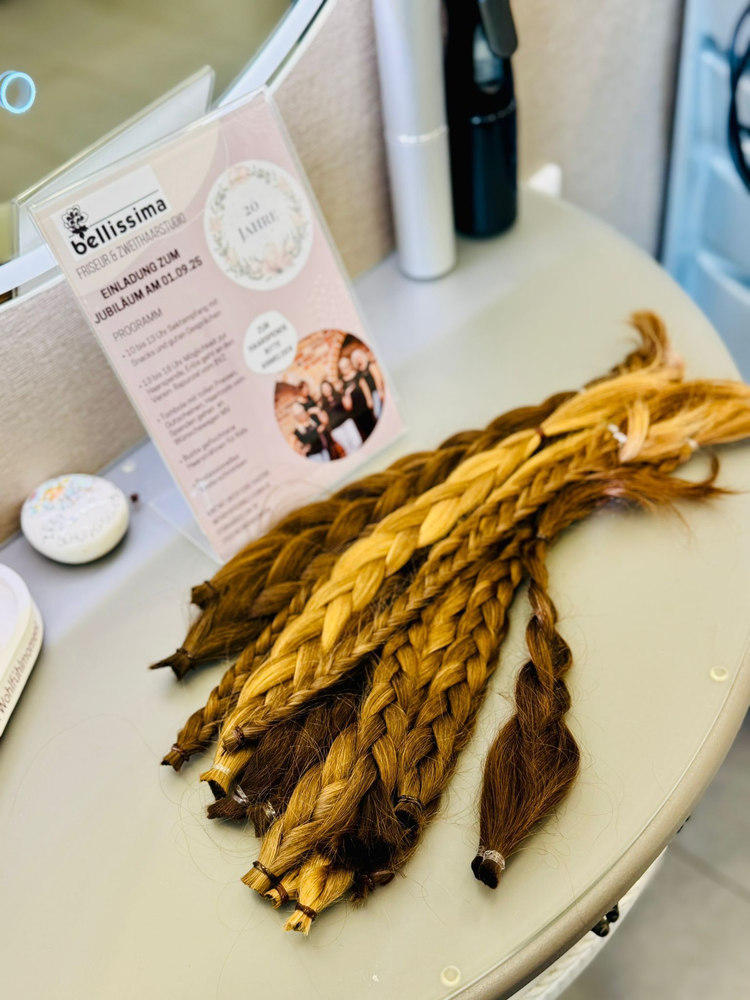 Geflochtene Haarverlängerungen in verschiedenen Braun- und Blondtönen, ausgestellt auf einem Salontisch neben einer Broschüre.
