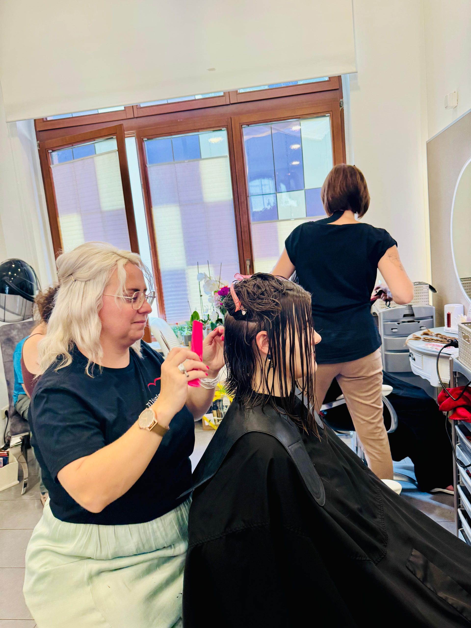 Eine Frau in einem Friseursalon lässt sich von einer anderen Frau, die rosa Kämme benutzt, die Haare stylen.