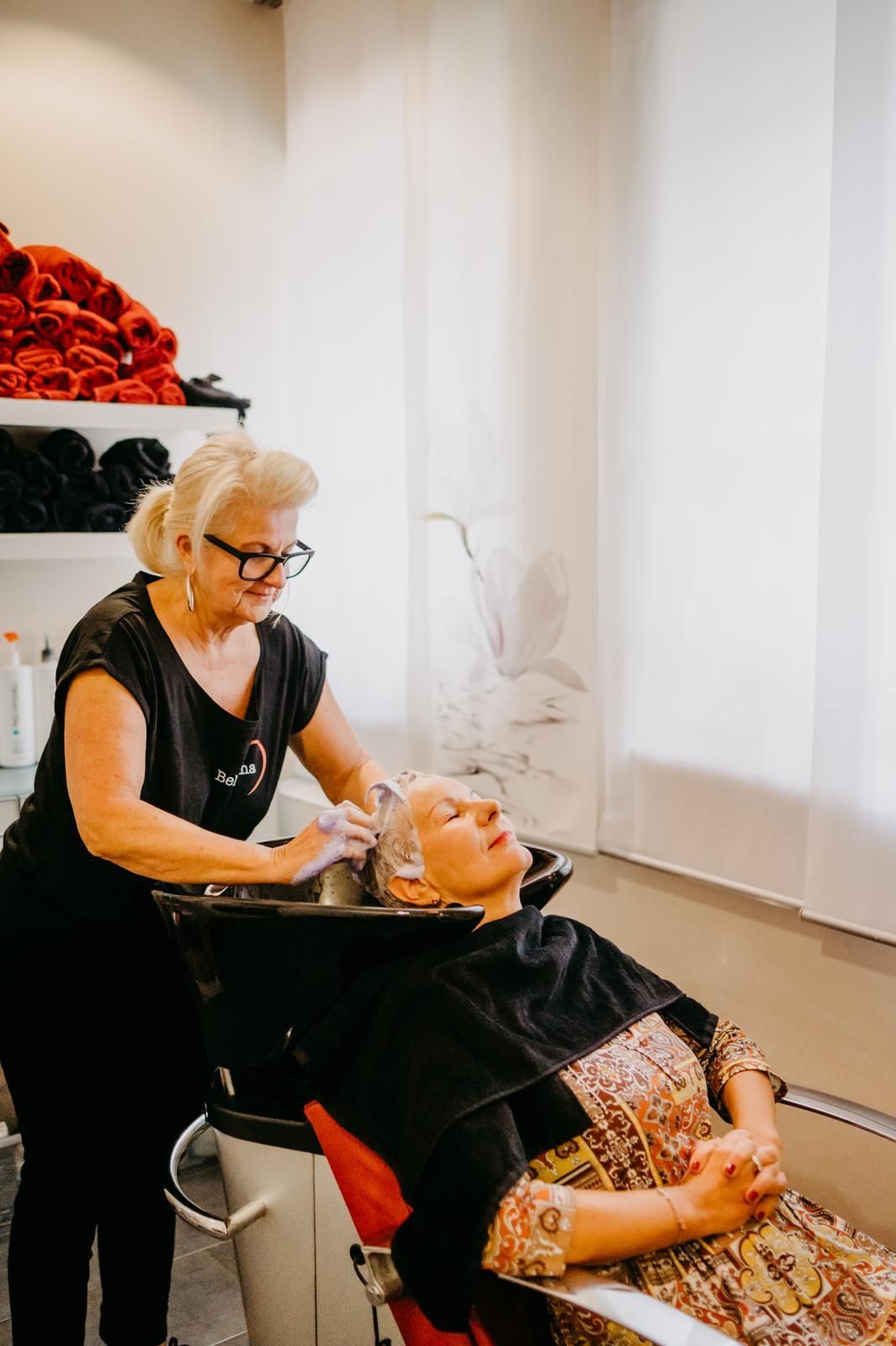 Eine Friseurin wäscht einer Kundin im Salon die Haare. Die Kundin sitzt entspannt auf einem Stuhl.