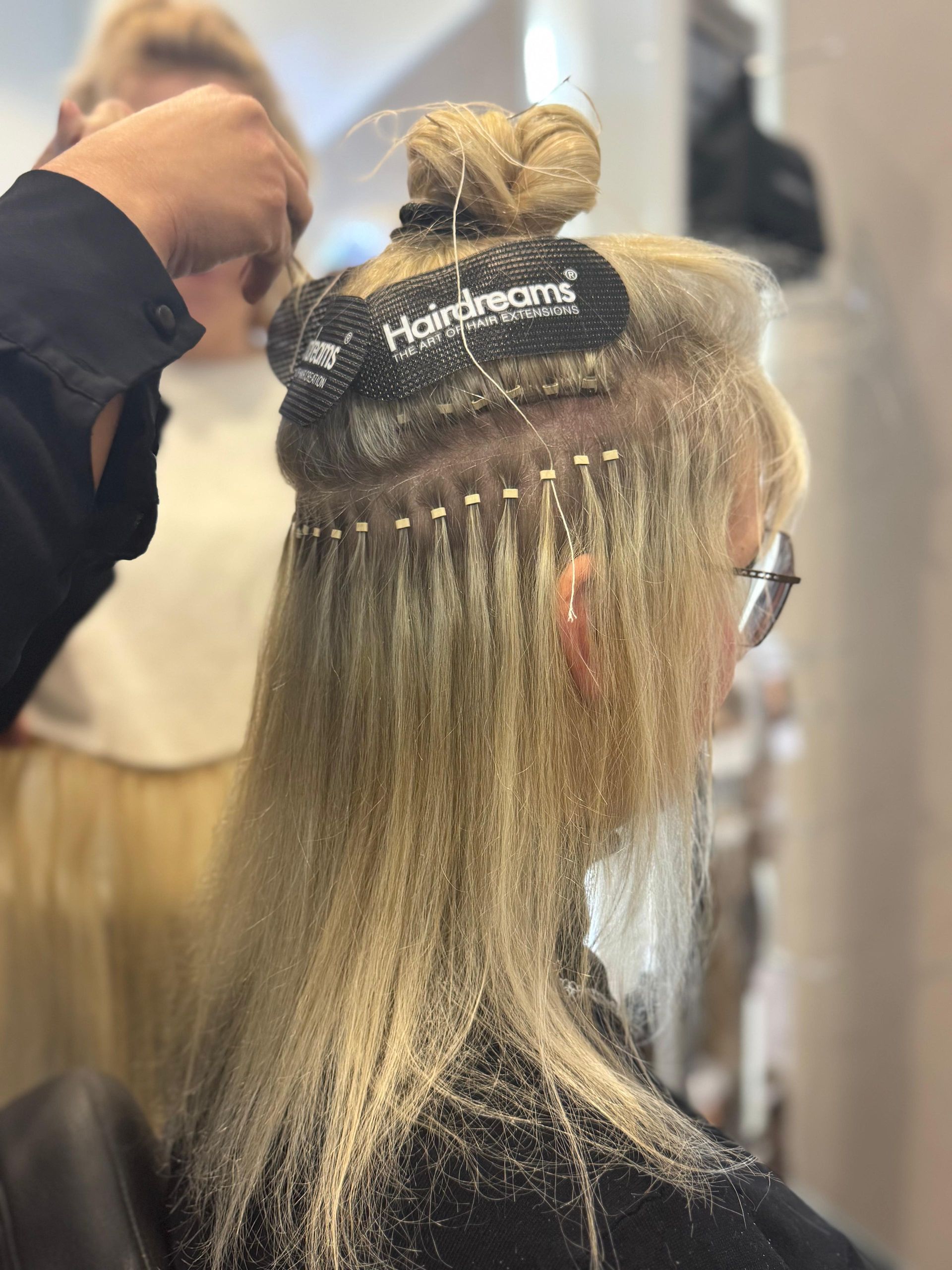 Eine blonde Frau lässt sich im Salon Haarverlängerungen machen. Die Extensions werden an ihrem natürlichen Haar befestigt.
