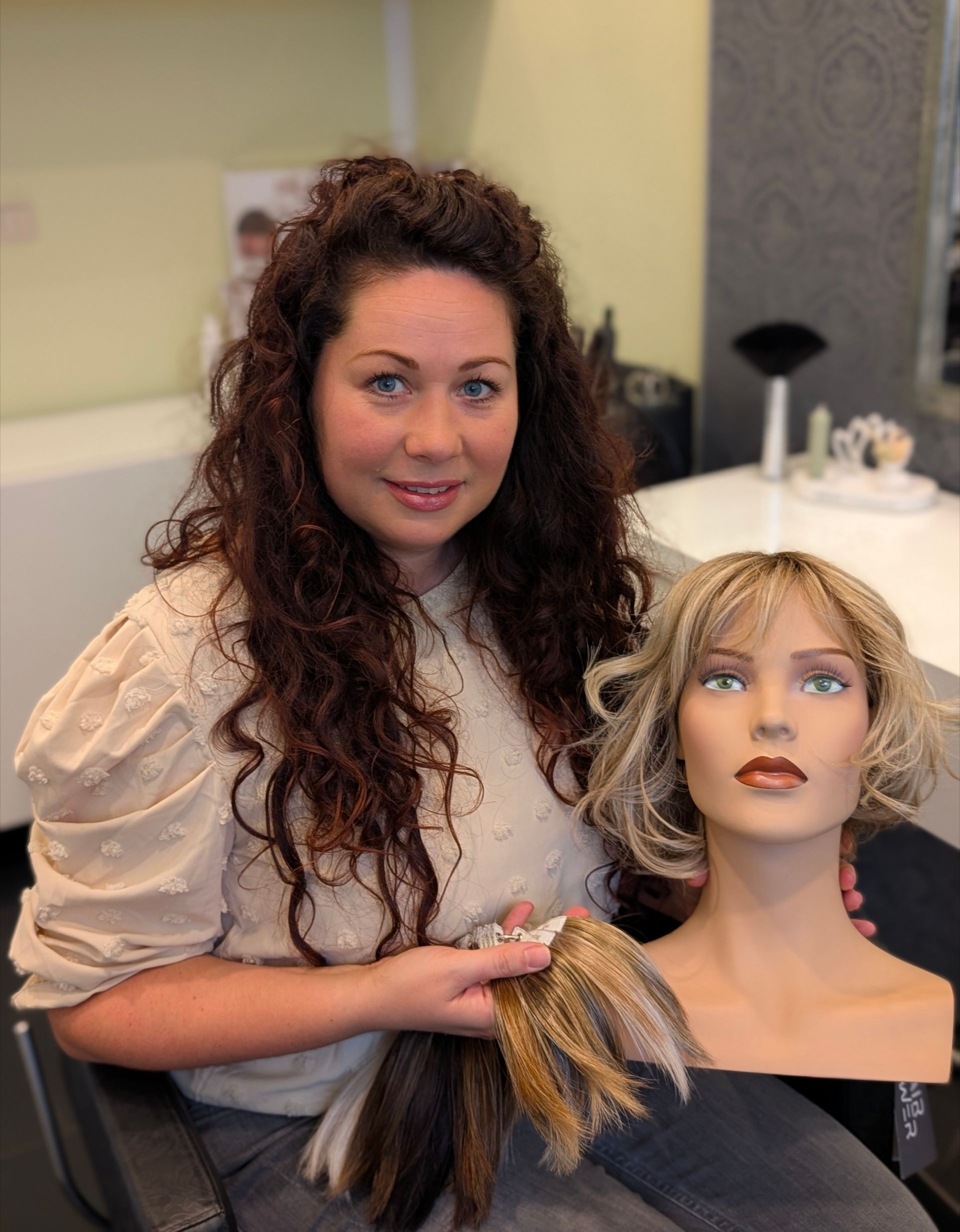 Eine Frau hält Haarproben neben einem Schaufensterpuppenkopf mit Perücke in einem Salon.