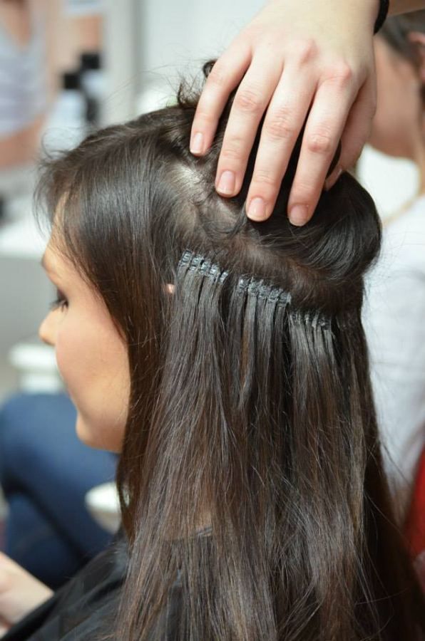 Haarverlängerungen werden in einem Salon an das natürliche Haar einer Frau angebracht.