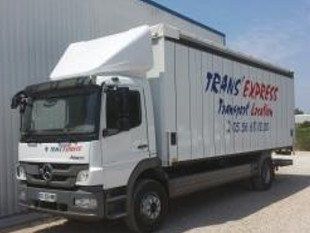 Camion blanc Trans Express garé à côté d'un bâtiment. Le logo sur le côté est en lettres bleues.