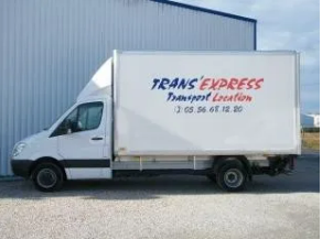 Camion de livraison blanc avec le logo « Trans'Express Transport Location » sur le côté. Stationné devant un immeuble.