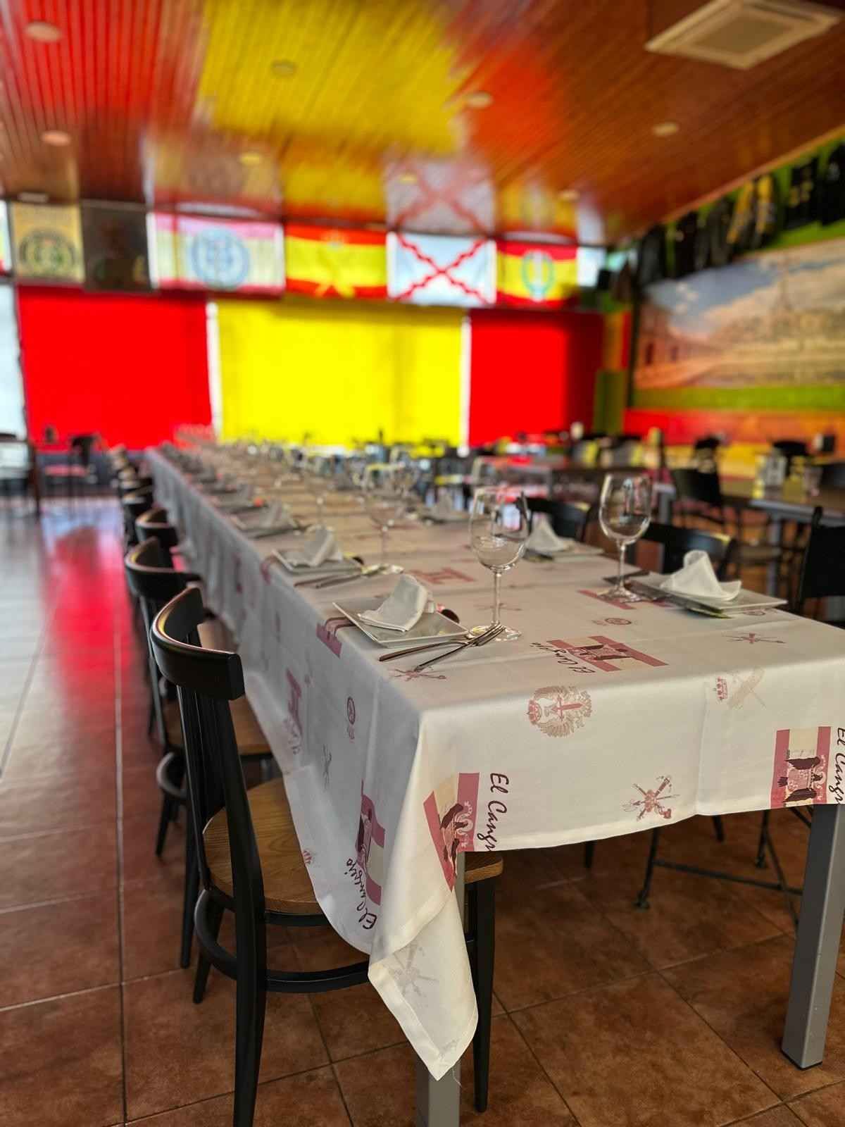 Una mesa redonda puesta para una comida formal con manteles blancos, sillas con fundas blancas, cubiertos y copas de vino.