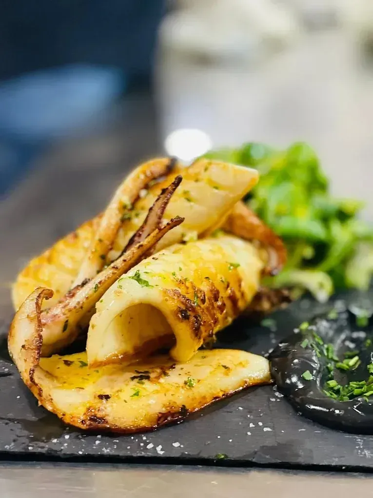 Calamares sellados servidos con una ensalada verde y salsa de tinta negra en un plato de piedra negra.