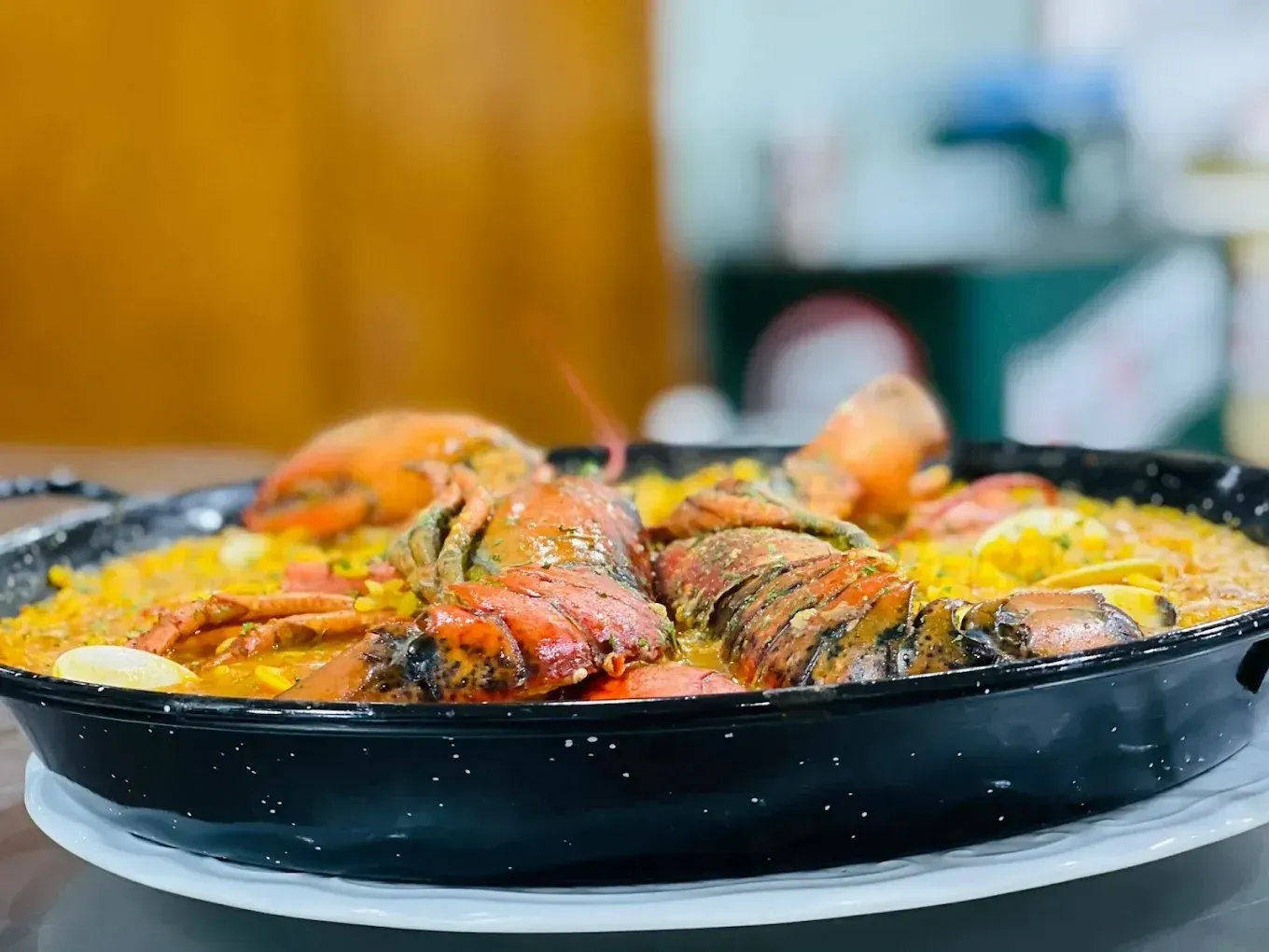 Sobre una mesa, una sartén negra llena de paella amarilla, cubierta con trozos de langosta cocida y ajo en rodajas.
