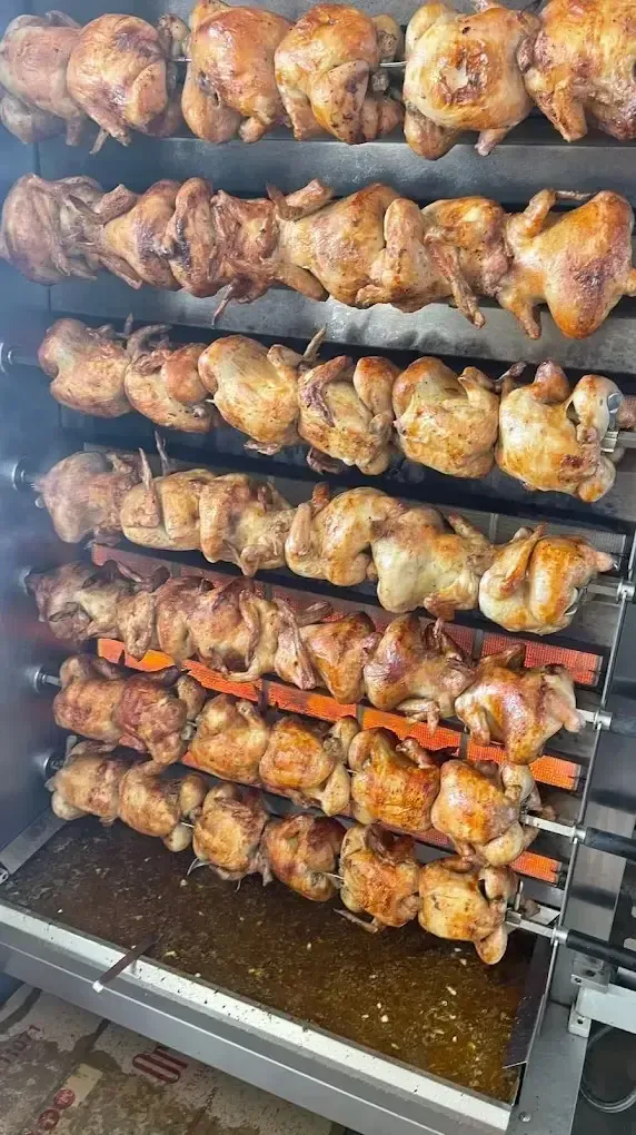 Hileras de pollos asados, dorados y crujientes, cocinándose en un asador metálico.