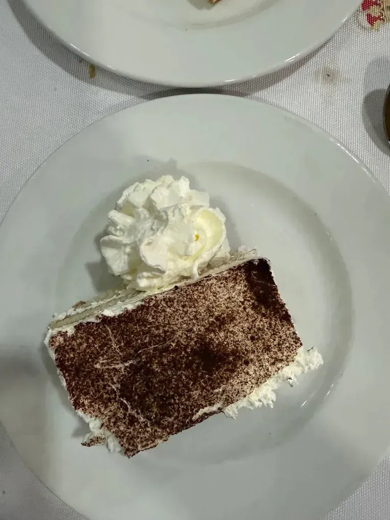 Una porción de tiramisú en capas, espolvoreada con cacao en polvo y servida en un plato blanco.