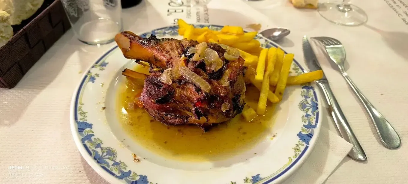 Un codillo de cerdo asado servido con patatas fritas en un plato blanco estampado en la mesa de un restaurante.