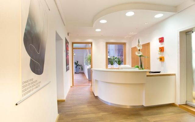Heller, moderner Empfangsbereich mit geschwungenem weißen Schreibtisch, Holzboden und Wandkunst