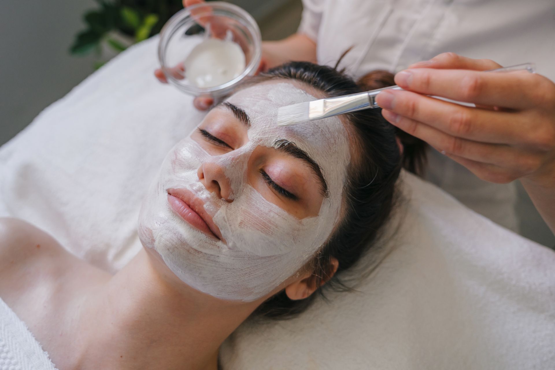 Soin du visage : une personne se fait appliquer un masque au pinceau tout en étant allongée sur un lit de spa.
