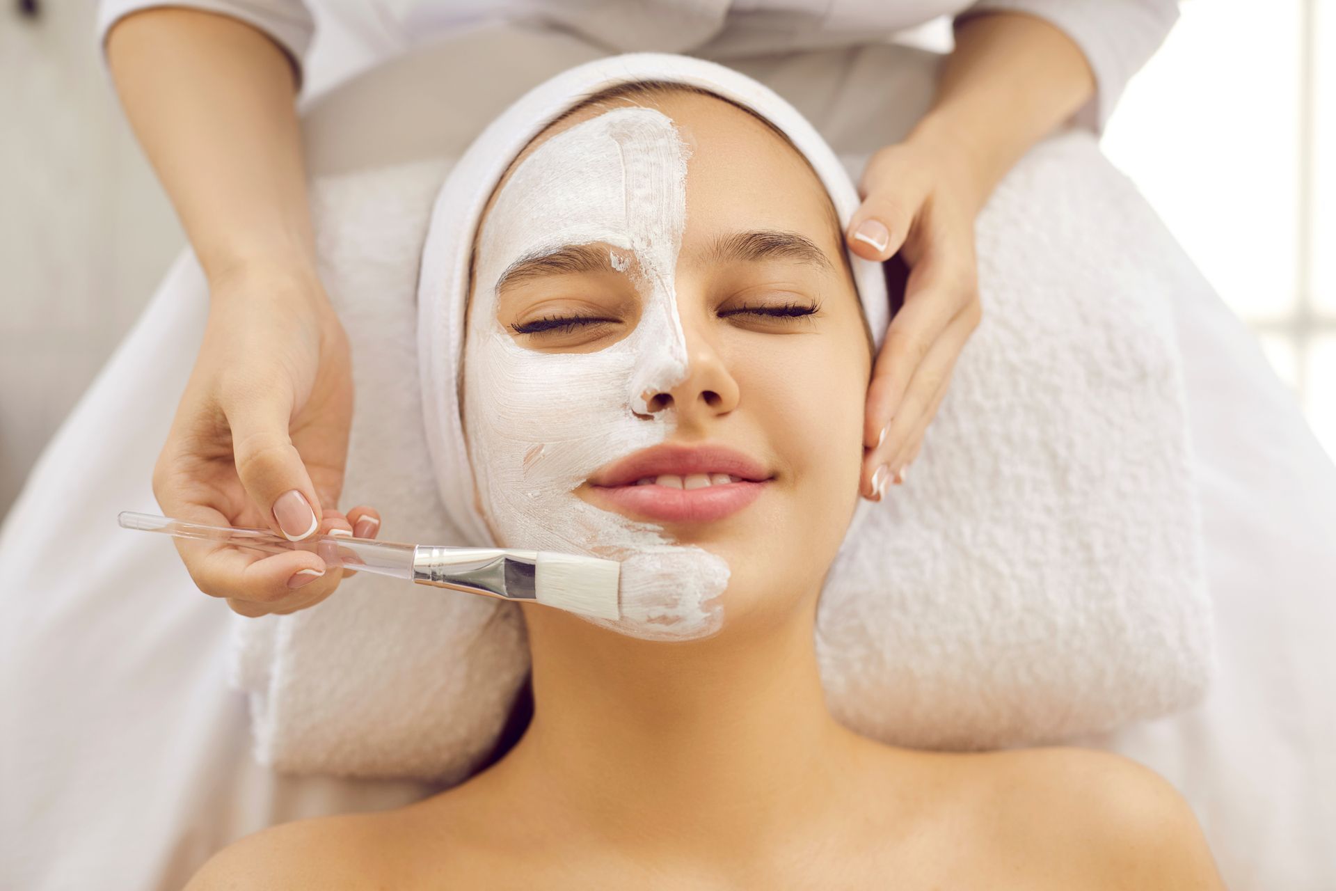 Femme se faisant appliquer un masque facial par une esthéticienne dans un spa.