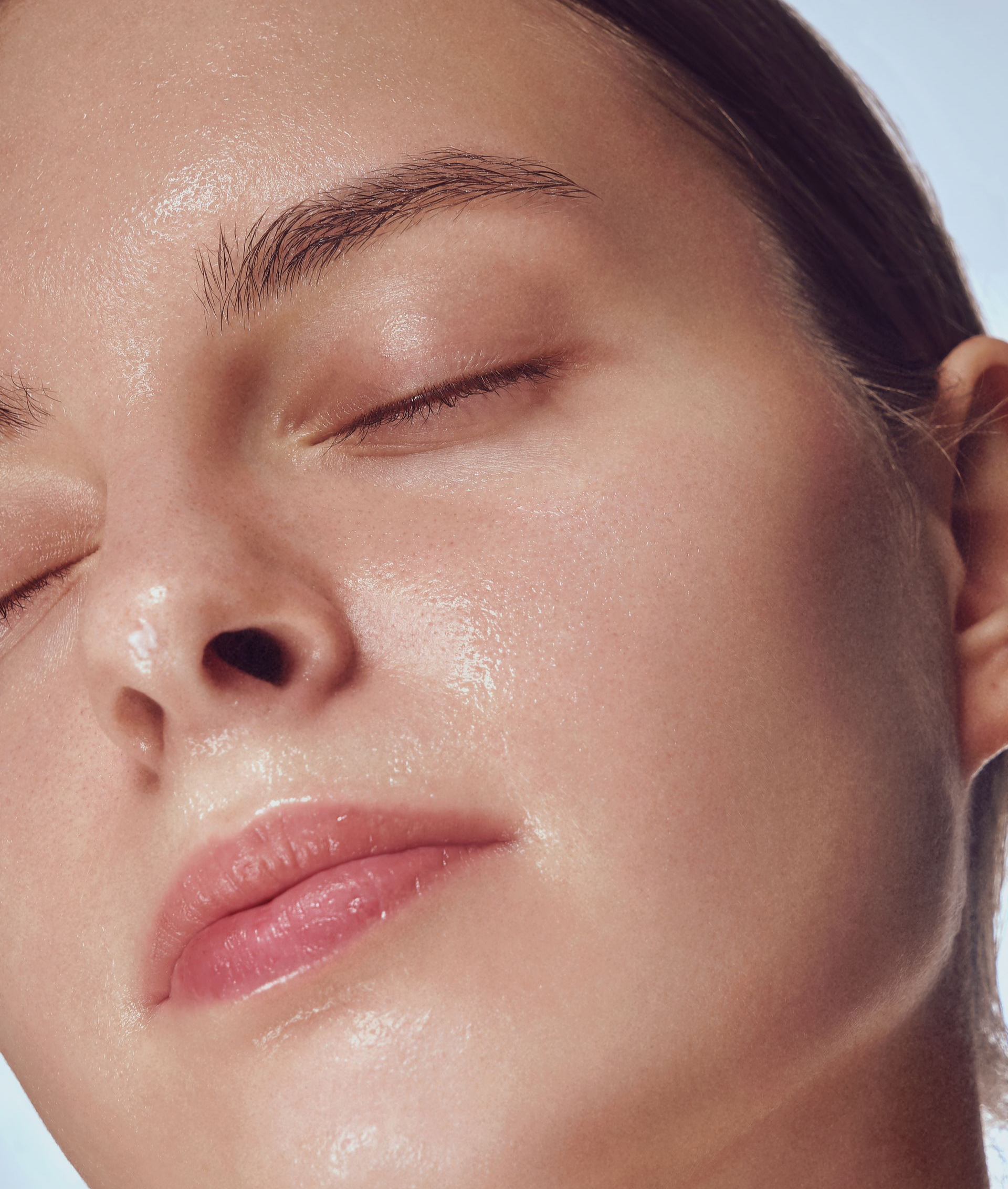 Gros plan sur le visage d'une personne aux yeux fermés ; la peau brillante suggère l'hydratation.