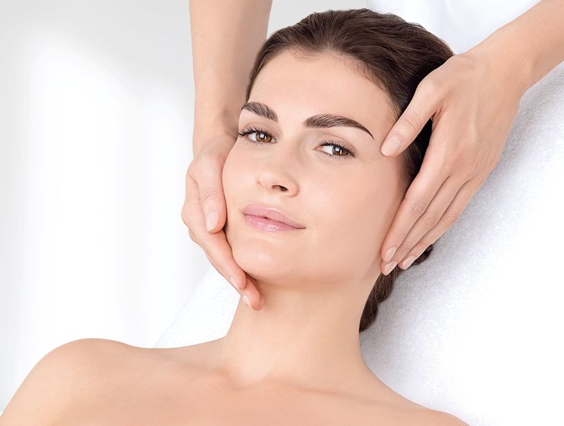 Une femme reçoit un massage du visage. Les mains sur son visage, expression douce.