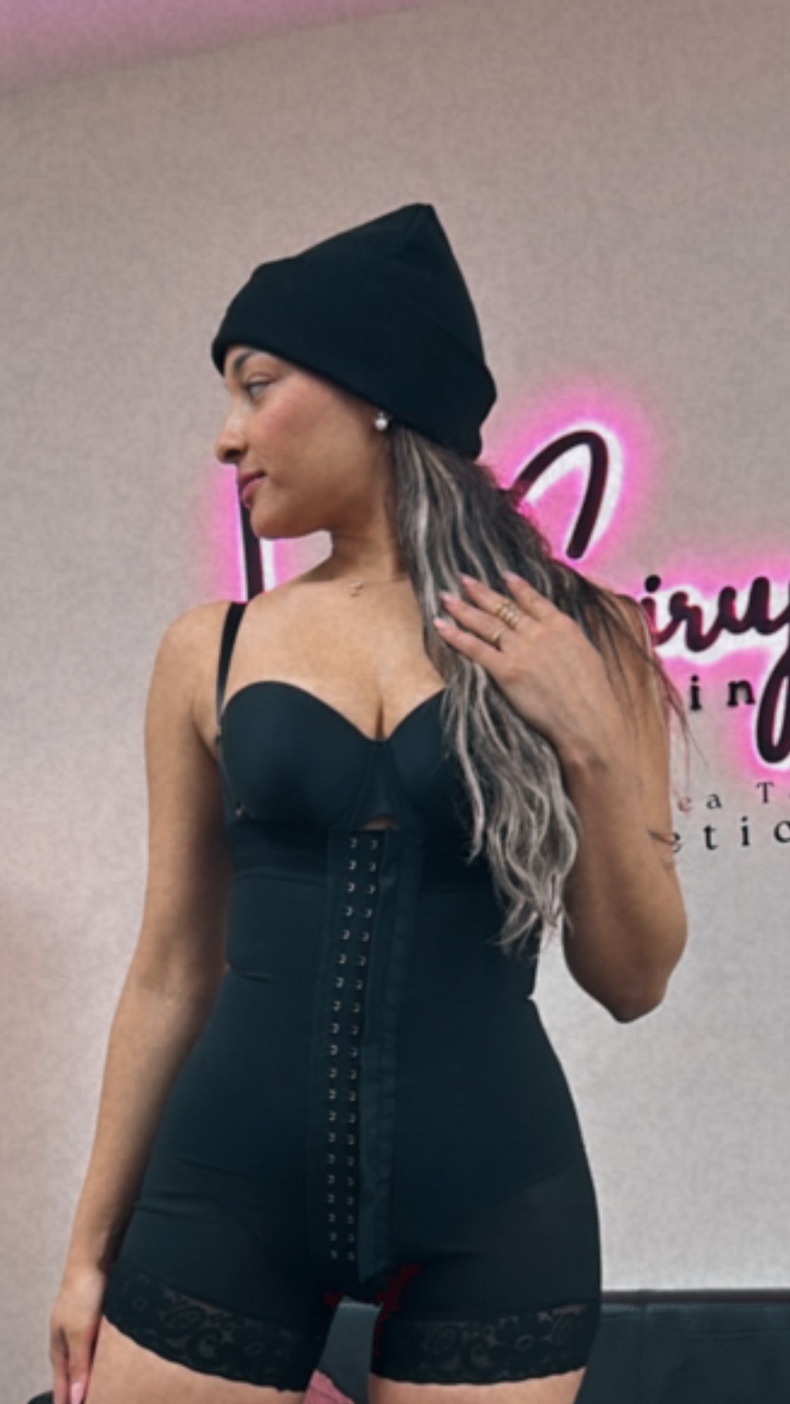 Una mujer que lleva un vestido negro y un sombrero negro está parada frente a un cartel rosa.