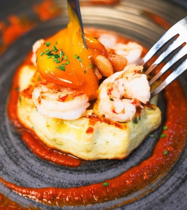 Camarones y salsa sobre una torta de papa frita cuadrada; tenedor en el plato, plato oscuro.