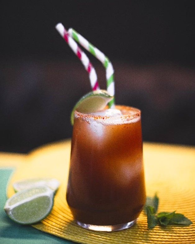 Cóctel en copa con pajitas rayadas de colores, guarnición de lima y líquido de color marrón rojizo.