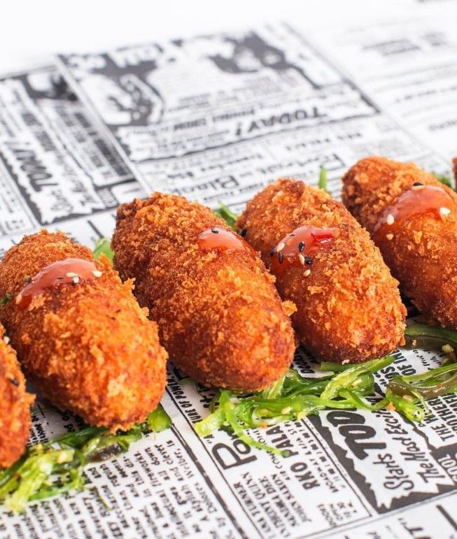Croquetas rebozadas con salsa roja sobre lecho de algas, servidas sobre papel de periódico.