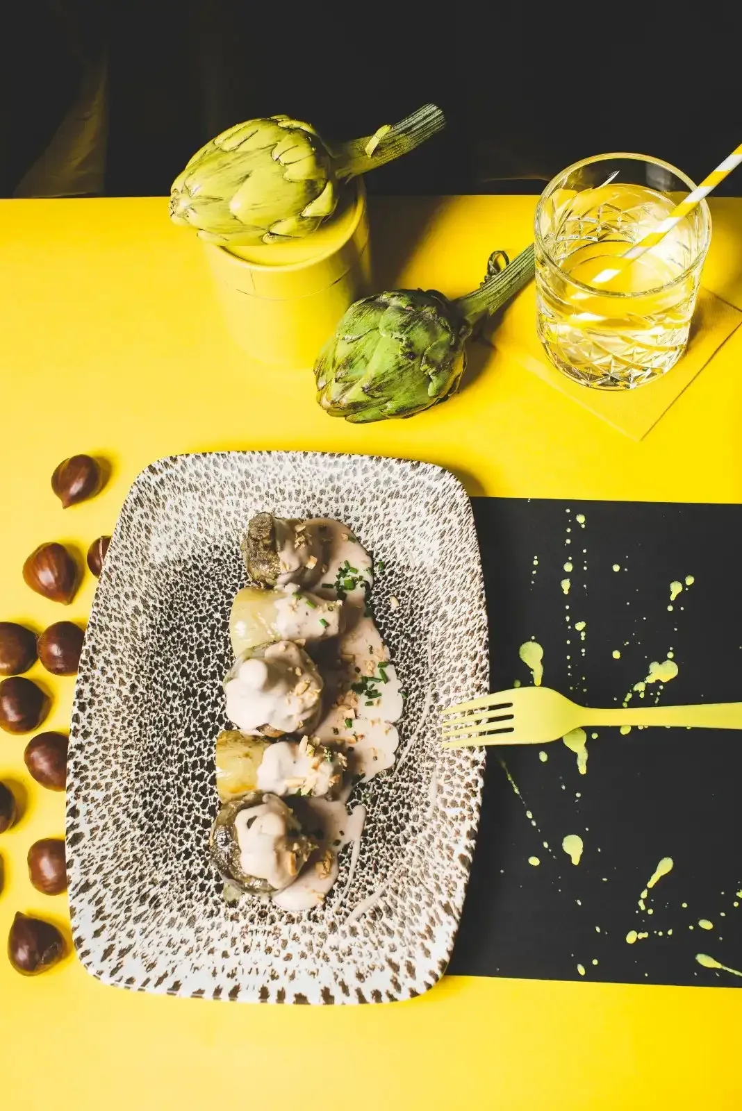 Plato de comida, bebida y alcachofas sobre una superficie amarilla y negra.