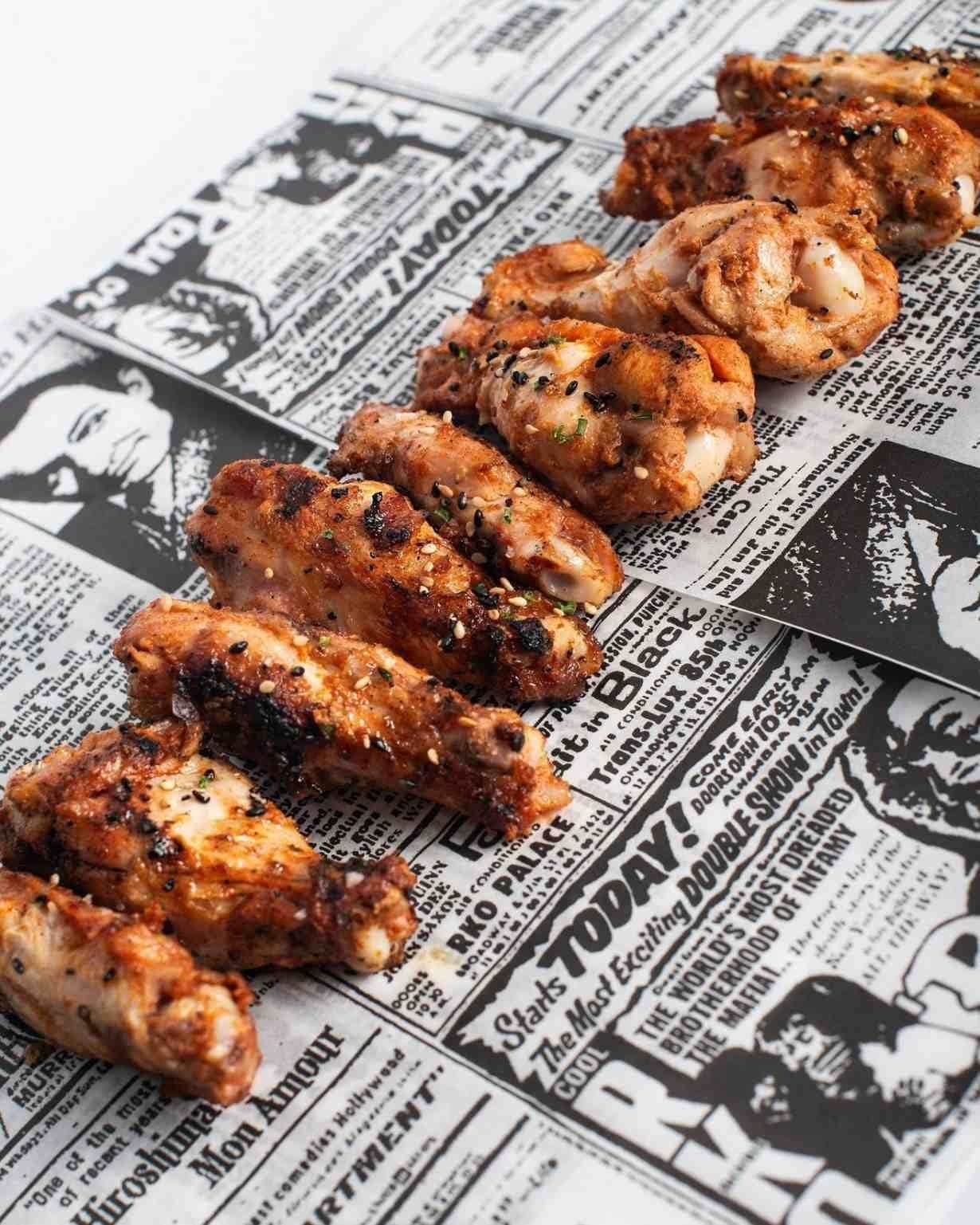 Alitas de pollo condimentadas con hierbas y semillas de sésamo sobre un papel de periódico.